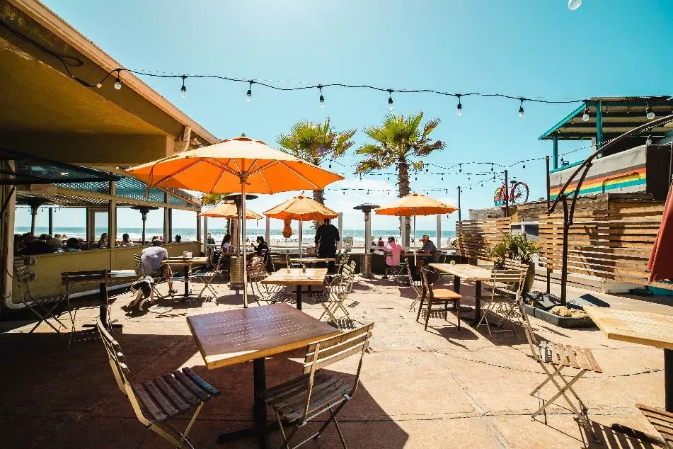 Outdoor restaurant patio with orange umbrellas overlooking a sunny beach.
