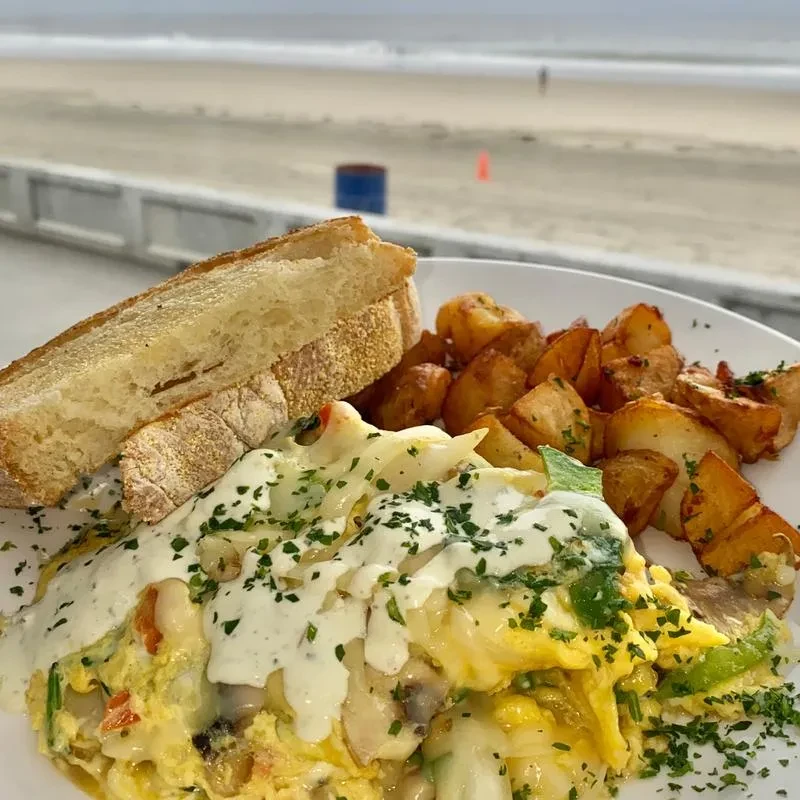 Plate of cheesy eggs, potatoes, and toast with a beach backdrop.