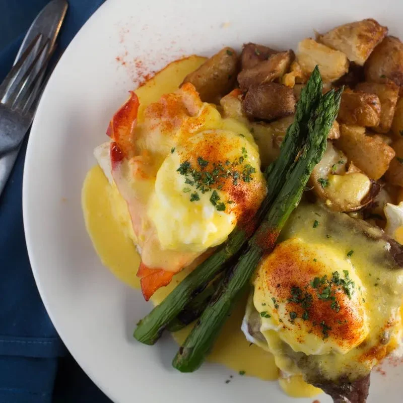 Top-down view of gourmet Eggs Benedict with lobster, asparagus, and potatoes.