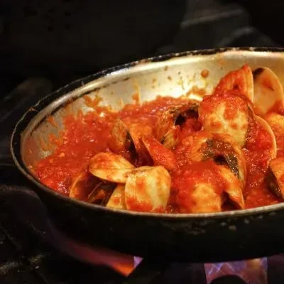 Rustic pan of clams simmering in red tomato sauce on stovetop.