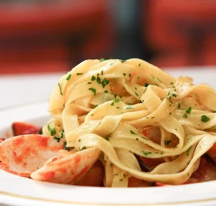 Pasta with seafood, parsley, and red sauce on white plate.