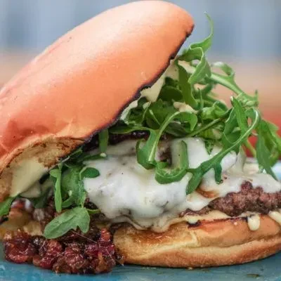 Close-up of a burger with melted cheese, beef patty, and arugula.