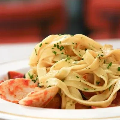 Tagliatelle-style pasta with red seafood and sprinkled green herbs.