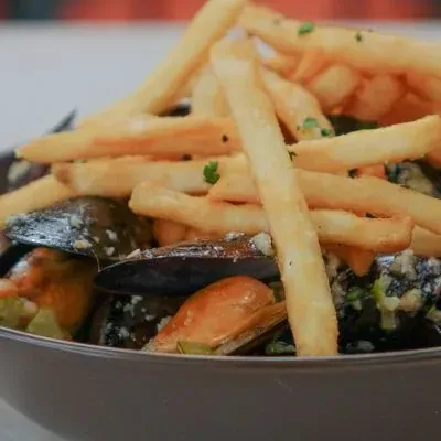 Mussels in sauce topped with golden, crispy french fries and herbs.