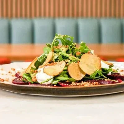 Plated arugula and beet salad with creamy dollops and nut garnish.