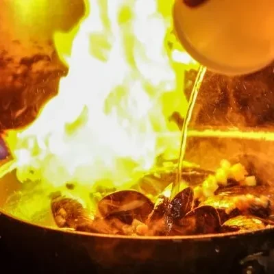 Flambéed shellfish in a pan with large, bright orange and yellow flames.