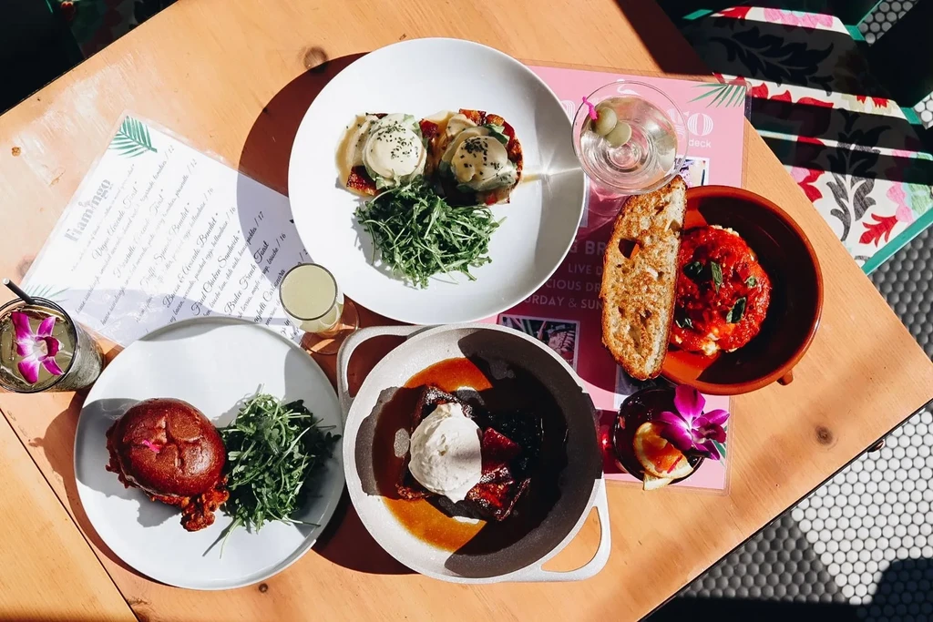 Sunlit restaurant table with diverse dishes, drinks, and a Flamingo menu.
