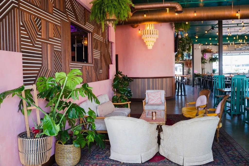 Eclectic restaurant interior with pink walls, lounge, and green plants.
