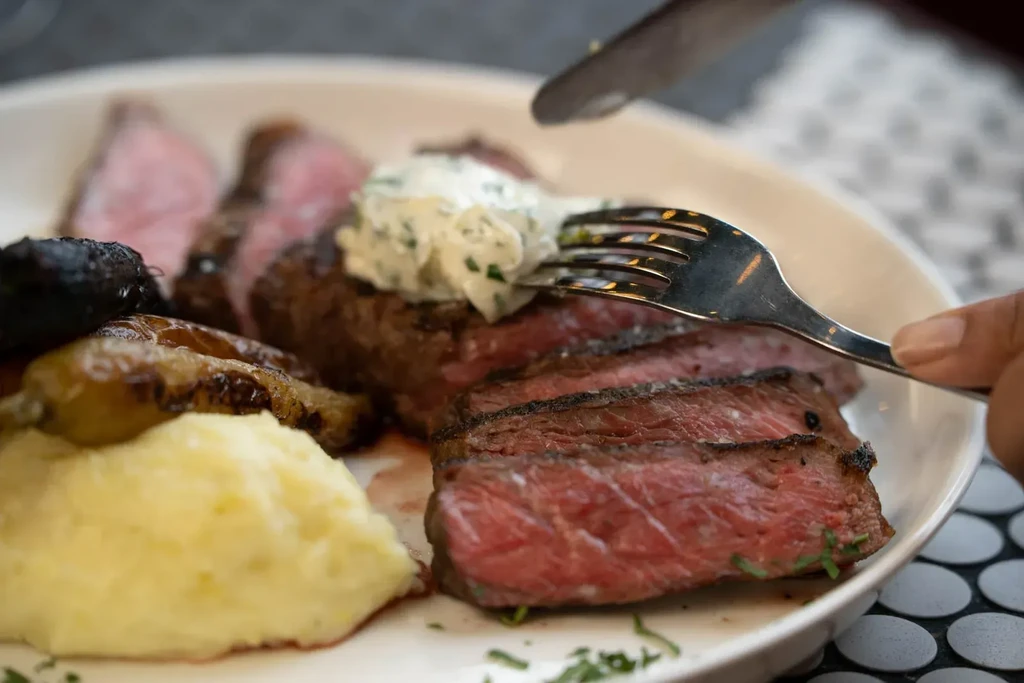 Sliced medium-rare steak, mashed potatoes, roasted vegetables on a white plate.