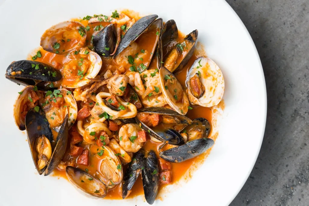 Vibrant seafood medley with tomato sauce and green herbs.