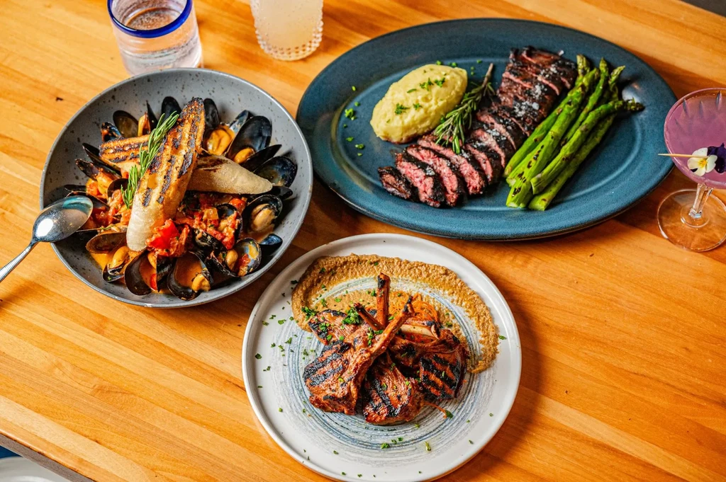 Overhead: Mussels, steak, lamb chops, and drinks on a wooden table.
