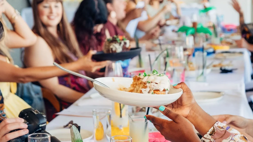 White food bowl with herbs held by hands, blurred social gathering.