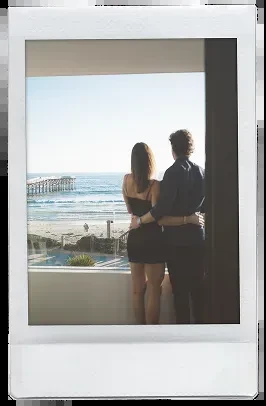 Couple with backs to viewer embracing, overlooking beach, ocean, pier.