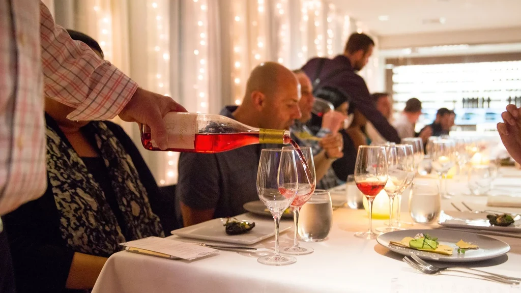 Hand pours red wine into a glass at a festive dining table.