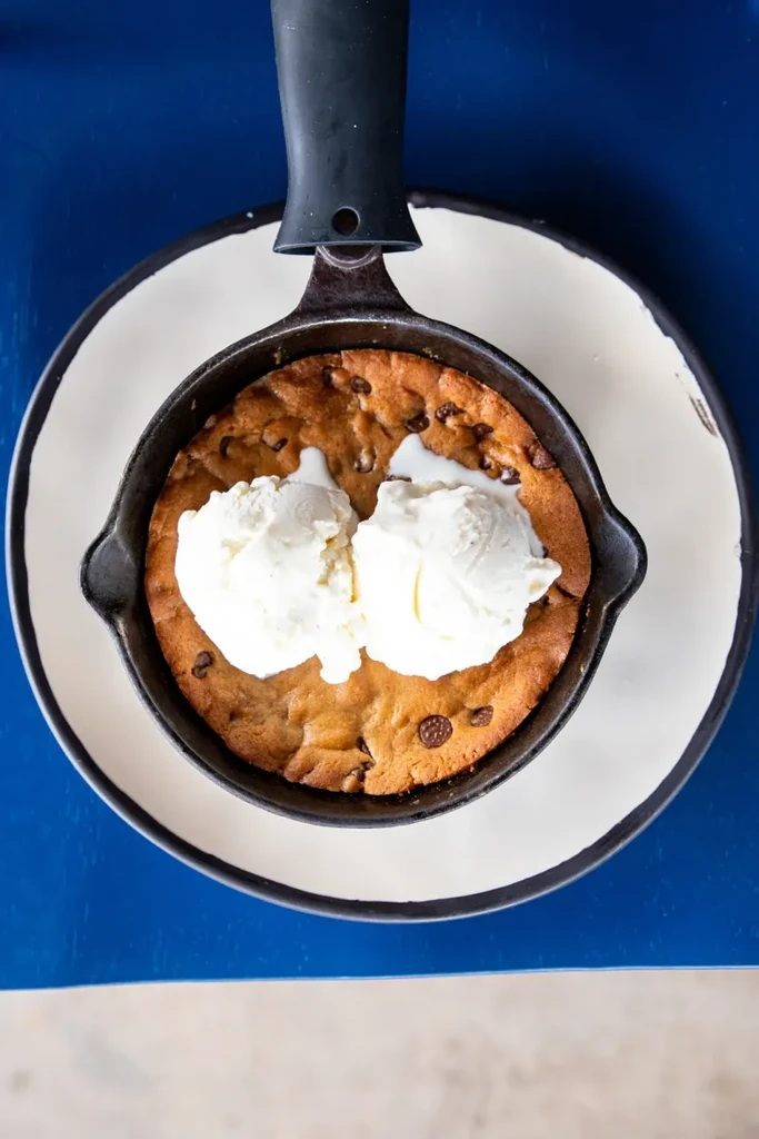 Warm chocolate chip cookie in cast-iron skillet with melting vanilla ice cream.
