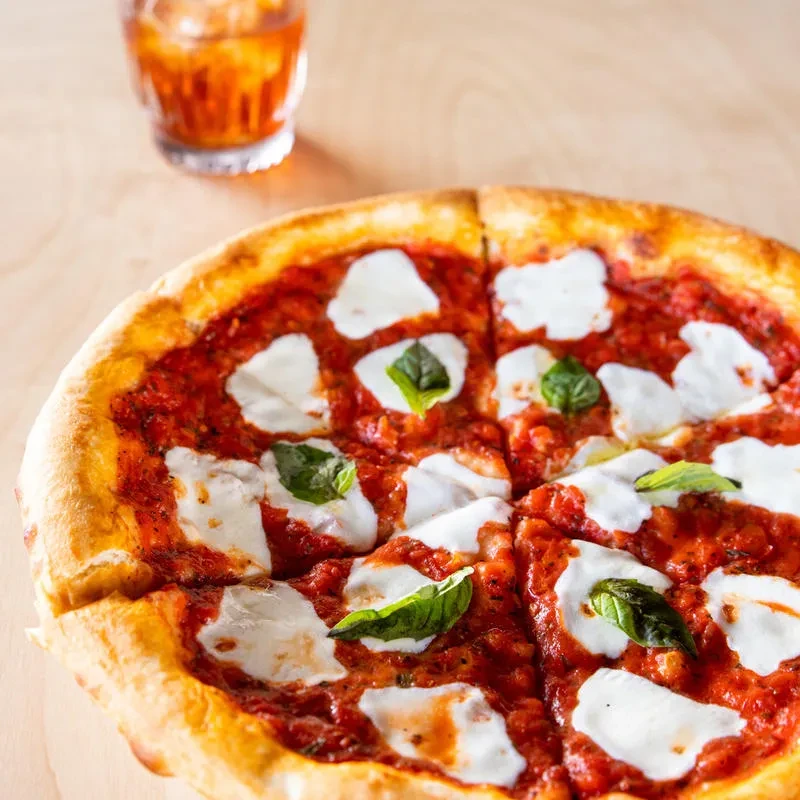 Sliced pizza with golden crust, mozzarella, basil, and a drink.