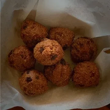 Eight golden-brown fried dough balls in a paper-lined container.