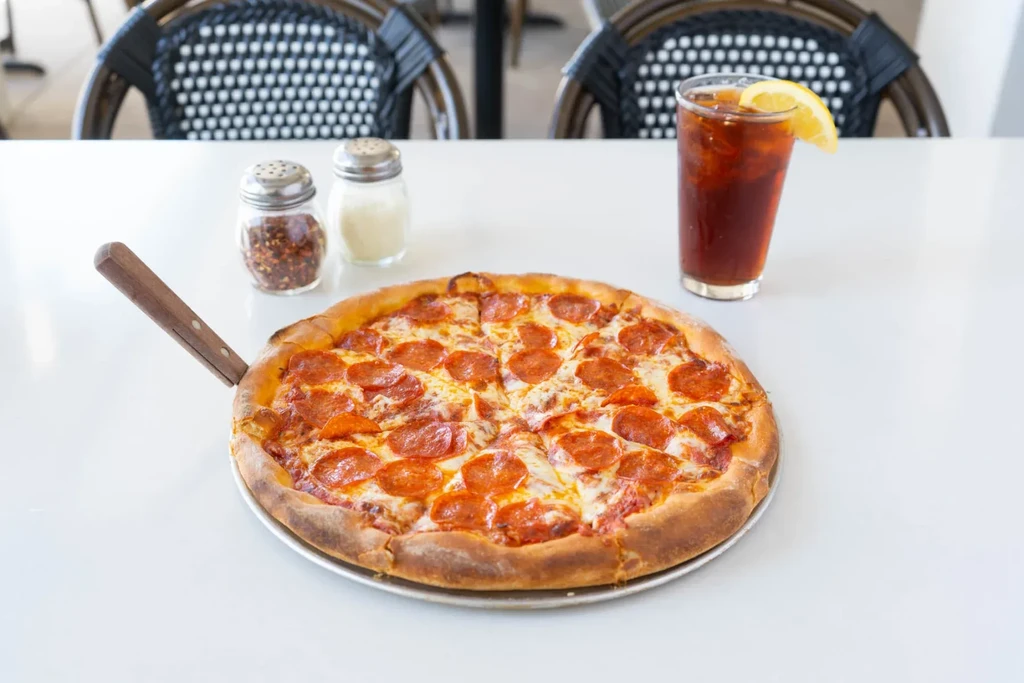 Sliced pepperoni pizza with red pepper, cheese shakers, and iced tea.