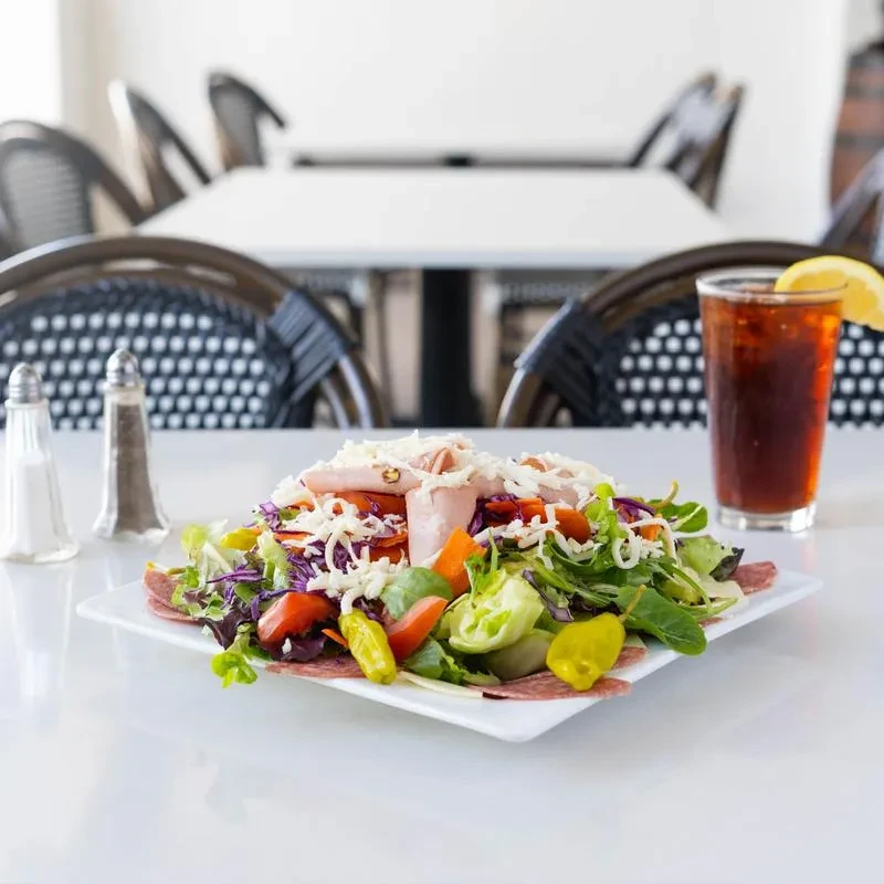 Large colorful salad with deli meats, cheese, and iced tea.