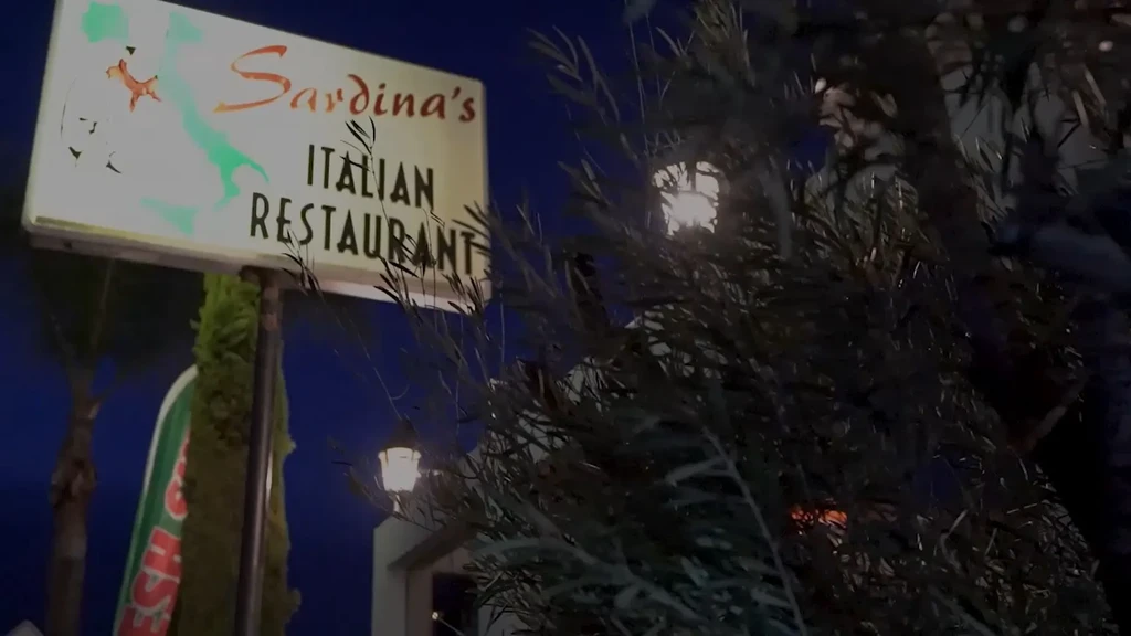 Illuminated Sardina's Italian Restaurant sign with fish and map, partly obscured.