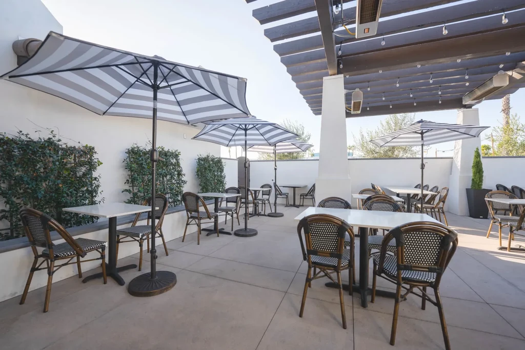 Outdoor restaurant patio with modern tables, chairs, umbrellas, and pergola.