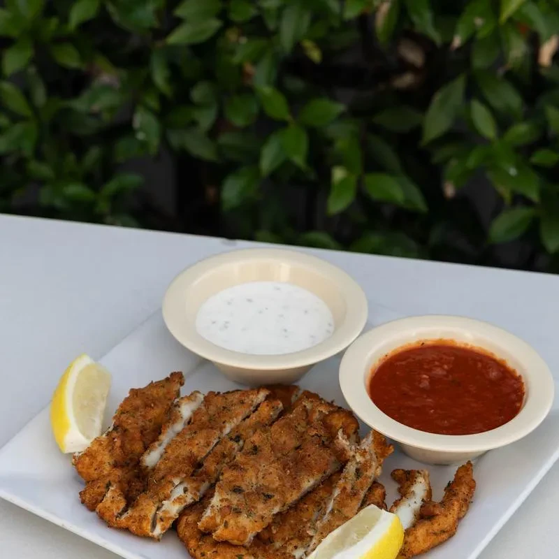 Golden fried strips with lemon and two dipping sauces, outdoors.