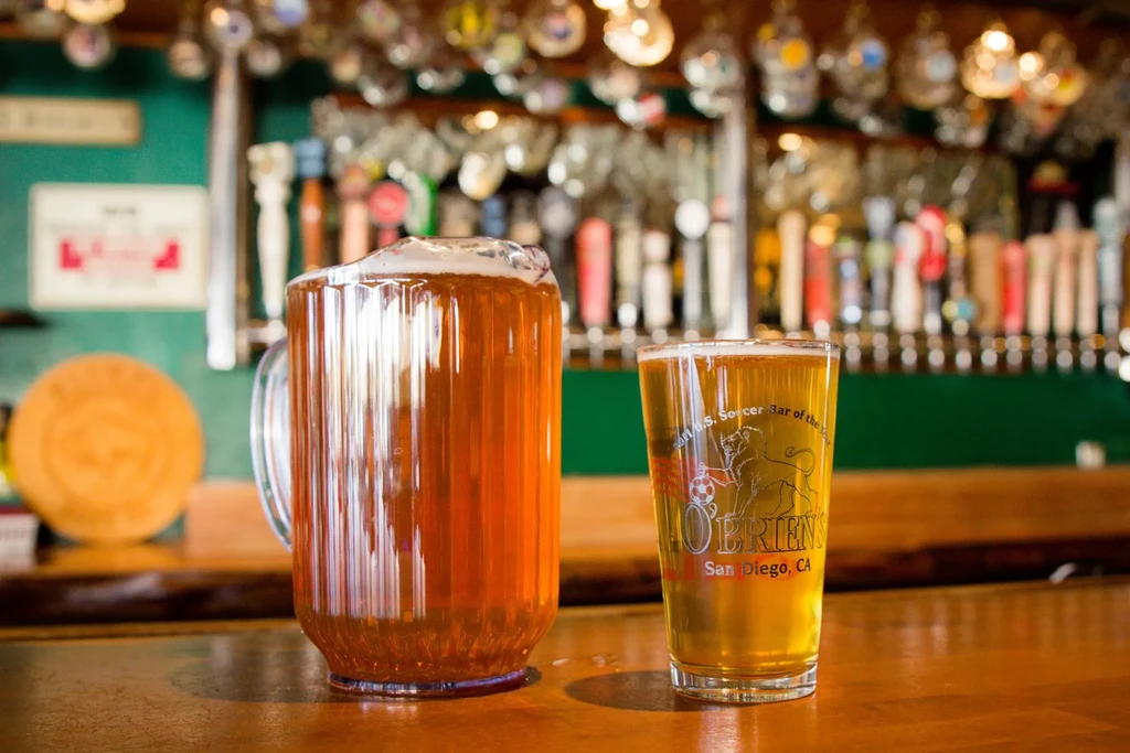 Amber beer in pitcher and O'Brien's pint glass on wooden bar.