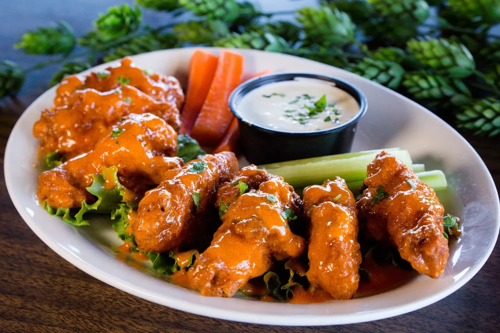 Plate of buffalo chicken wings, celery, carrots, and creamy dipping sauce.