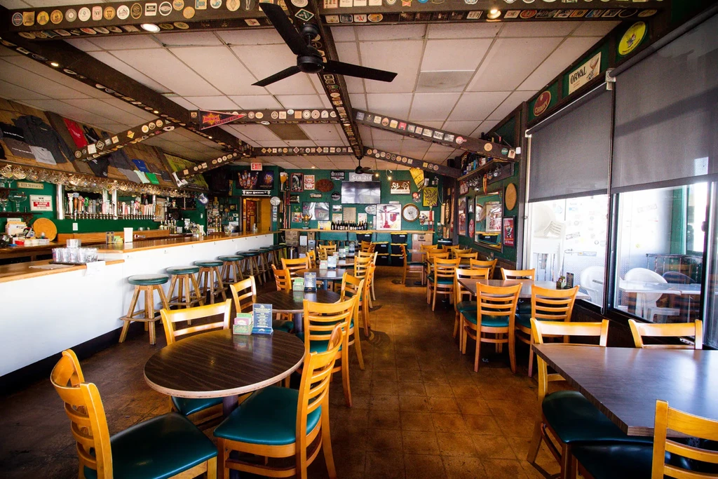 Bar interior with long wooden bar, green stools, and decorated green walls.