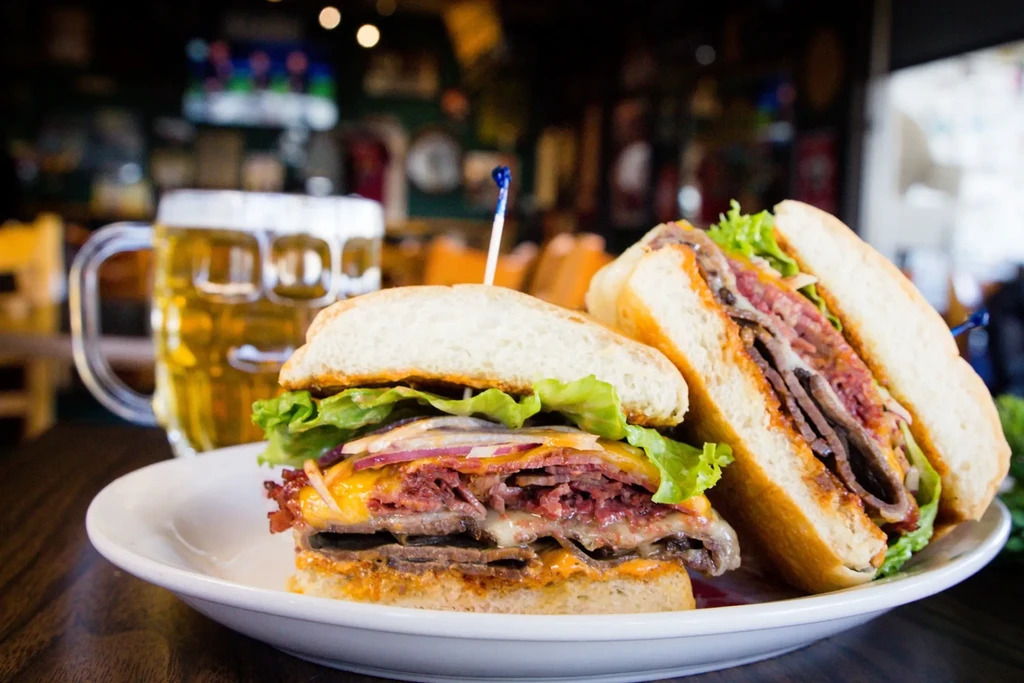 Close-up pastrami or Reuben sandwich cut in half with beer.