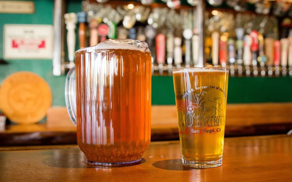 Pitcher and O'Brien's branded beer pint on a wooden bar.
