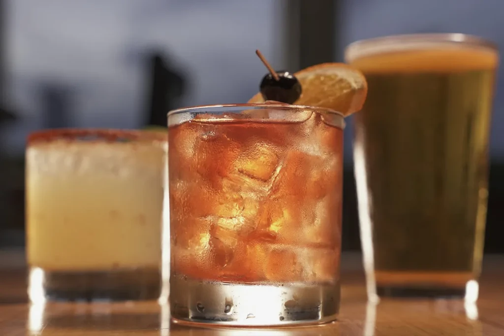 Frosted Old Fashioned, a beer, and a yellow cocktail on a bar.