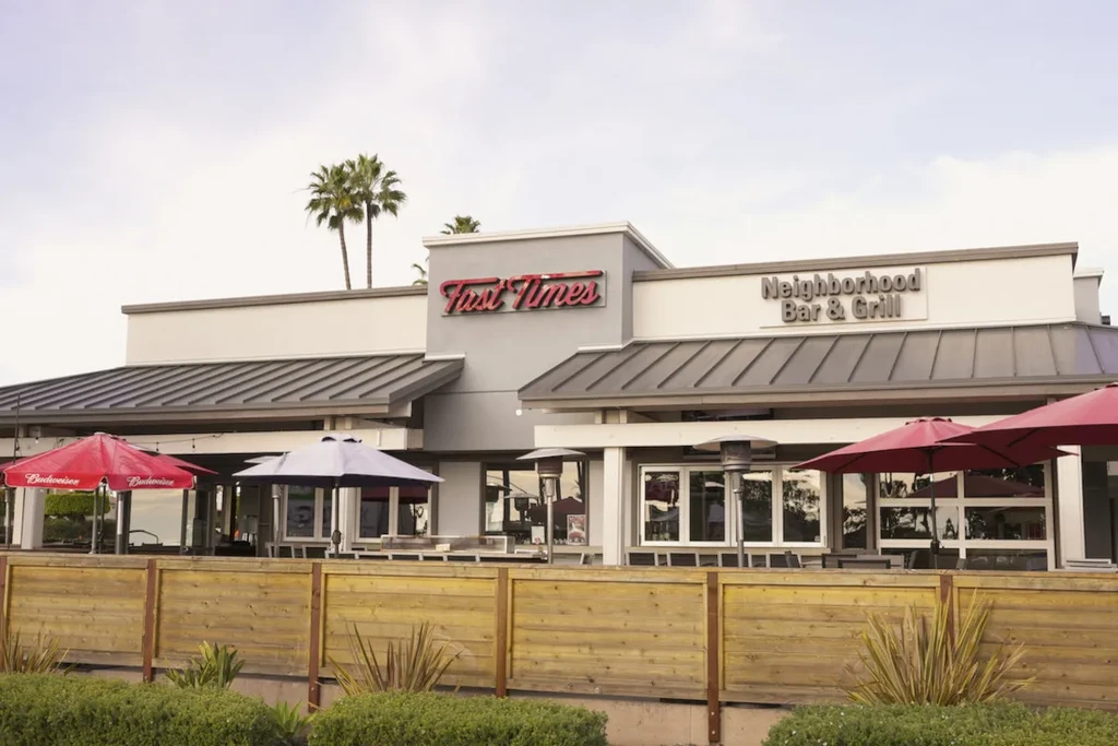 Modern grey Fast Times Bar & Grill exterior with patio, Budweiser umbrellas.