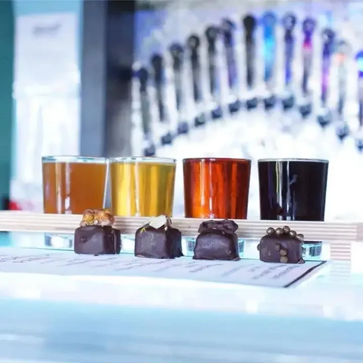 Beer flight with chocolates on a blue-lit tray at a bar.