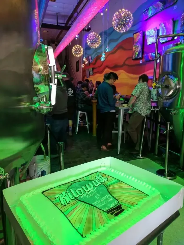 Kilowatt Brewing anniversary cake in a colorful industrial brewery with tanks.