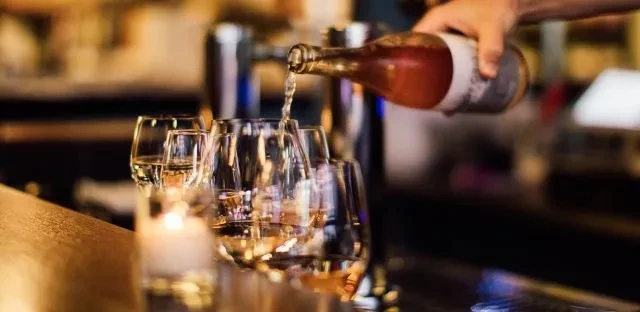 Hand pouring rosy beverage from amber bottle into wine glasses.