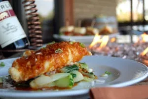 Fish with reddish-orange sauce, green onions, and green vegetables.
