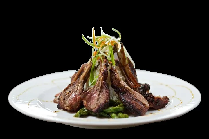 Medium-rare lamb chops with green vegetables and onions on white plate.