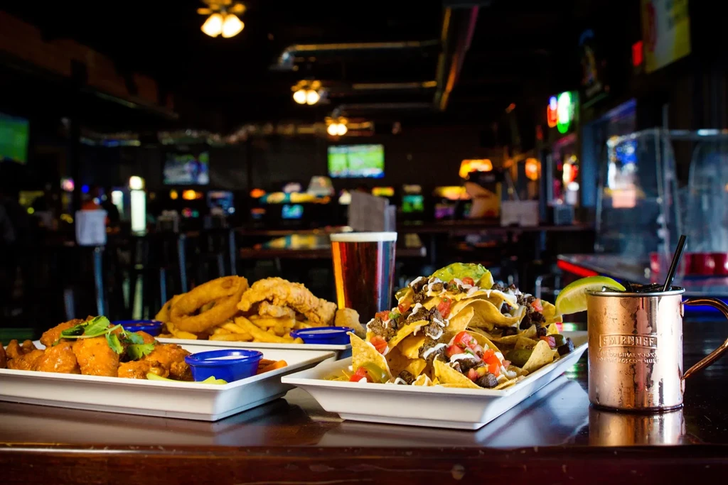 Nachos, wings, fries, beer, and a cocktail on a bar counter.