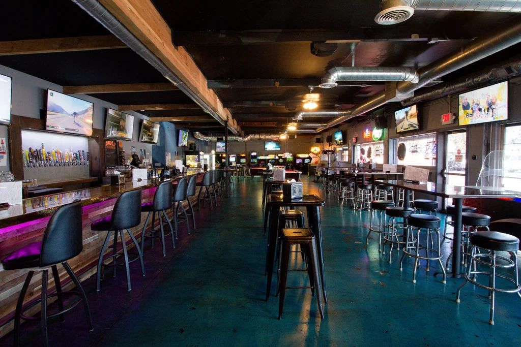 Empty arcade bar with purple-lit tap bar, TVs, and games.