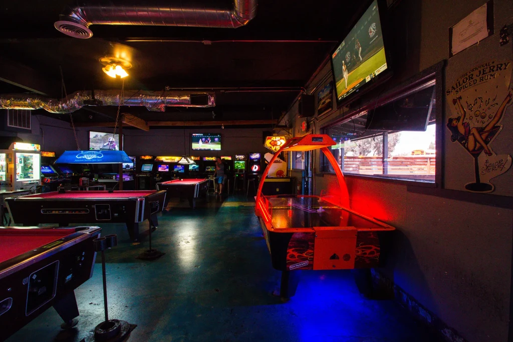 Arcade bar with pool, glowing air hockey, and colorful arcade machines.