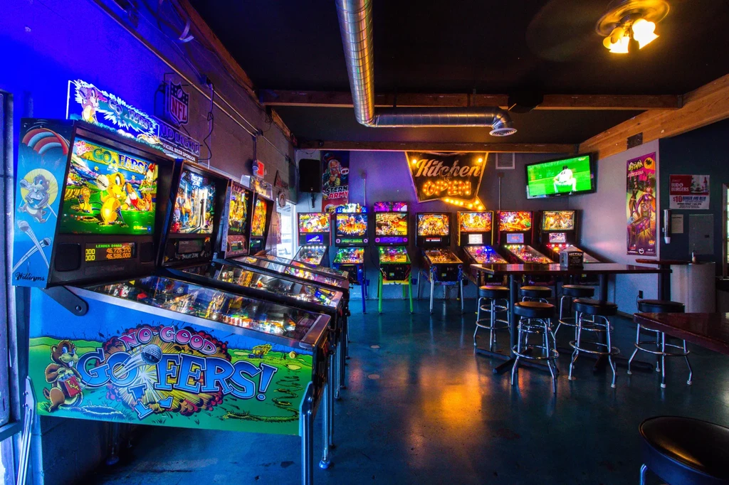 Illuminated pinball machines line a dimly lit arcade bar interior.