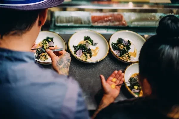 Two chefs carefully plating small, elegant dishes at a high-end counter.