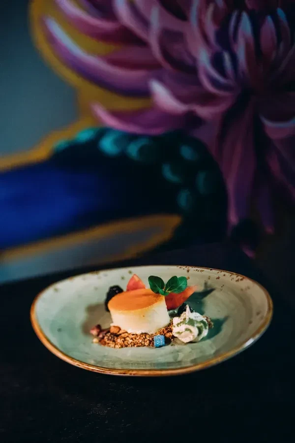Cylindrical panna cotta dessert with fruit, mint, granola, and blue object.