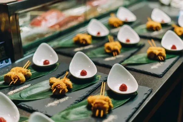Fried food skewers, green leaf, red sauce on individual slate plates.
