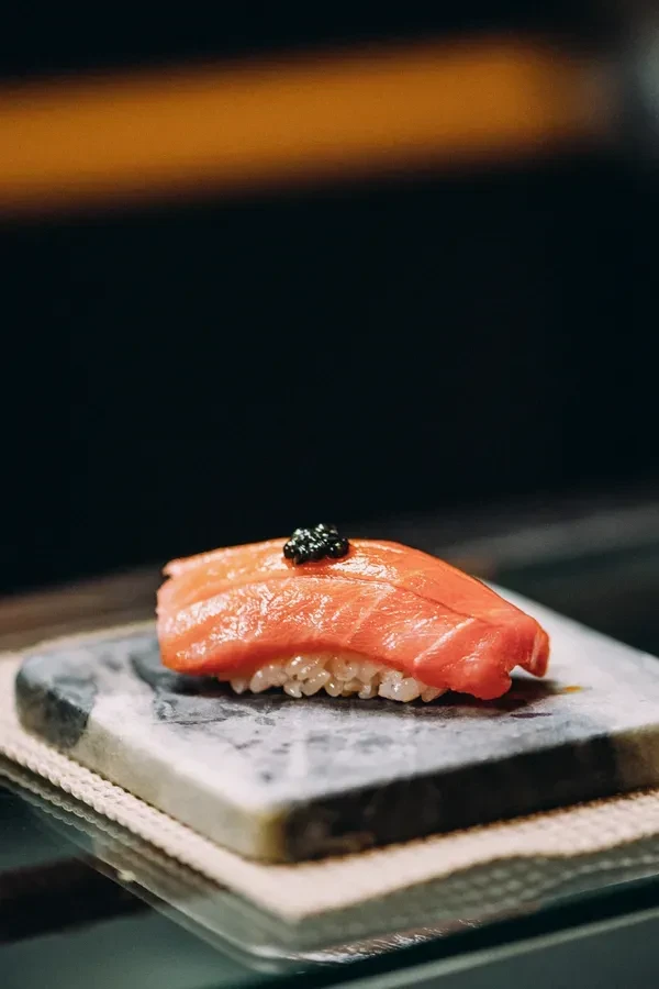 Reddish-pink tuna nigiri topped with black caviar on a stone slab.
