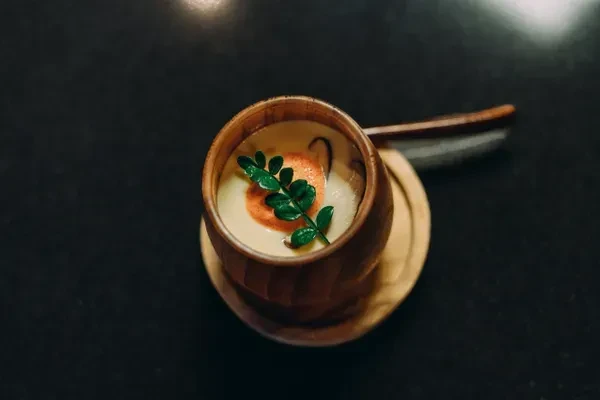 Elegant small dish in ribbed wooden cup with orange and green garnish.