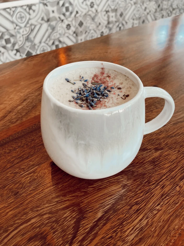 White mug with foamed drink, garnished with lavender and pink powder.