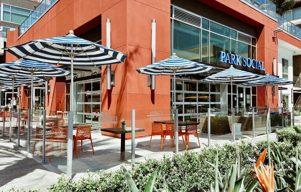Modern restaurant 'PARK SOCIAL' with orange facade, patio, and striped umbrellas.