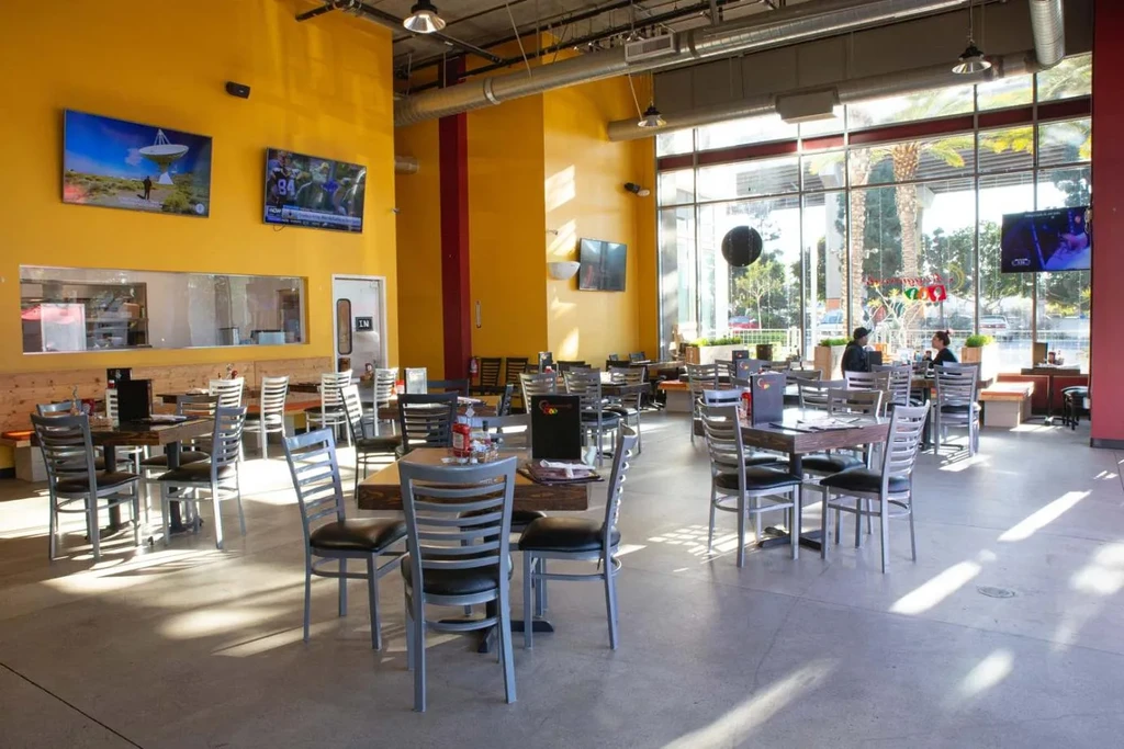 Modern restaurant interior with yellow walls, tables, and industrial ceiling.